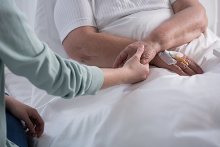 Gros plan sur une personne soignante ou un proche tenant chaleureusement la main d'un patient âgé allongé dans un lit d'hôpital, équipé d'un cathéter intraveineux.