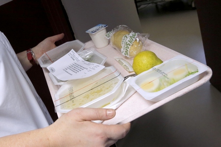 Plateau repas composé de plusieurs récipients scellés pour conserver la chaleur (on devine des oeufs durs et de la soupe). Il y a aussi une poire, du pain, un yaourt et un bulletin sur lequel est indiqué le menu, le numéro de la chambre et le régime suivi.