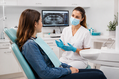 consultation : une dentiste portant un masque et des gants stériles s'entretient avec une patiente assise sur un fauteuil de dentiste afin de préparer les soins